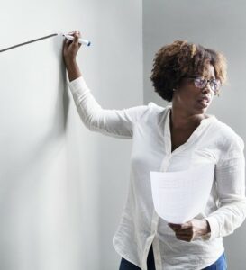 Woman at white board with marker in one hand and notes in the other 