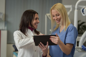 A practice manager talking with a vet/tech in scrubs with a tablet in her hand