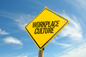 Un cartel amarillo que dice Cultura en el lugar de trabajo sobre un fondo de cielo azul