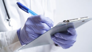 Close-up of a doctor writing a prescription in a medical record on a tablet. A doctor in a white coat and gloves is writing a prescription with a blue pen. Medical banner concept.