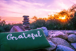 A pillow that says grateful with a carin and sunset behind it.