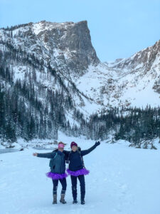 Duas alpinistas femininas posando em frente a um lago alpino congelado de neve