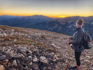 Uma alpinista de pé em uma montanha olhando para o nascer do sol
