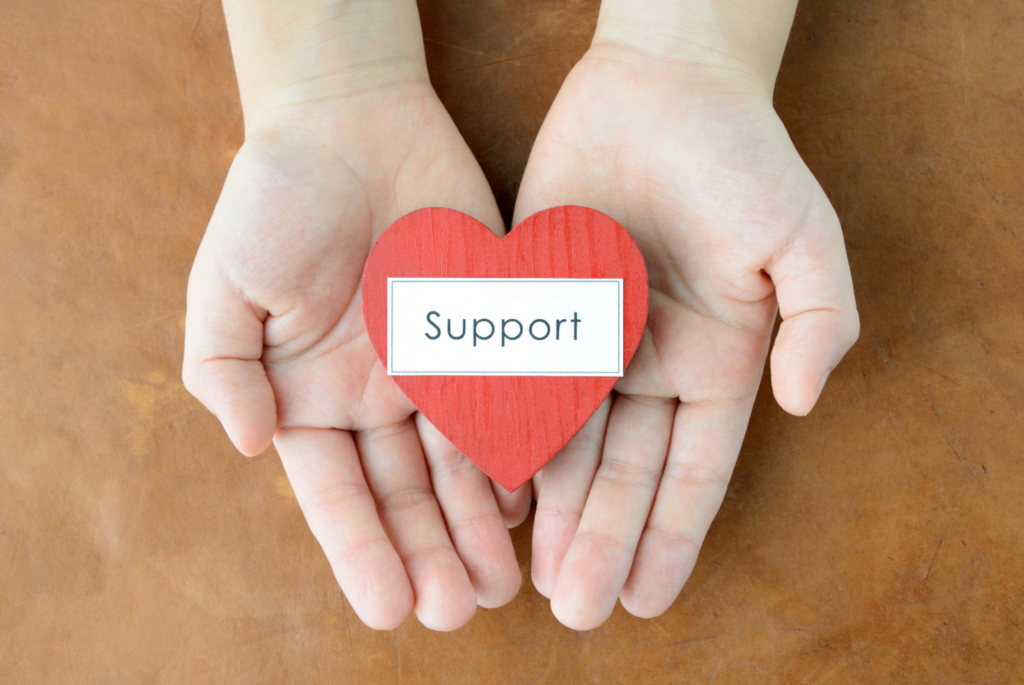 A person holding a red heart in their hands that says "Support".
