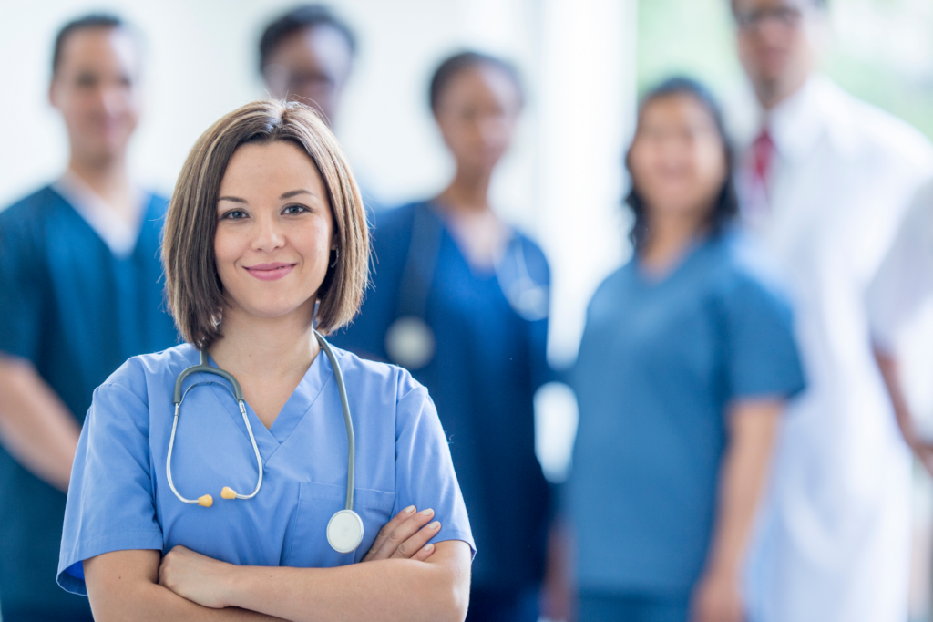 A female in scrubs standing out in front a team of people that are not in focus. 